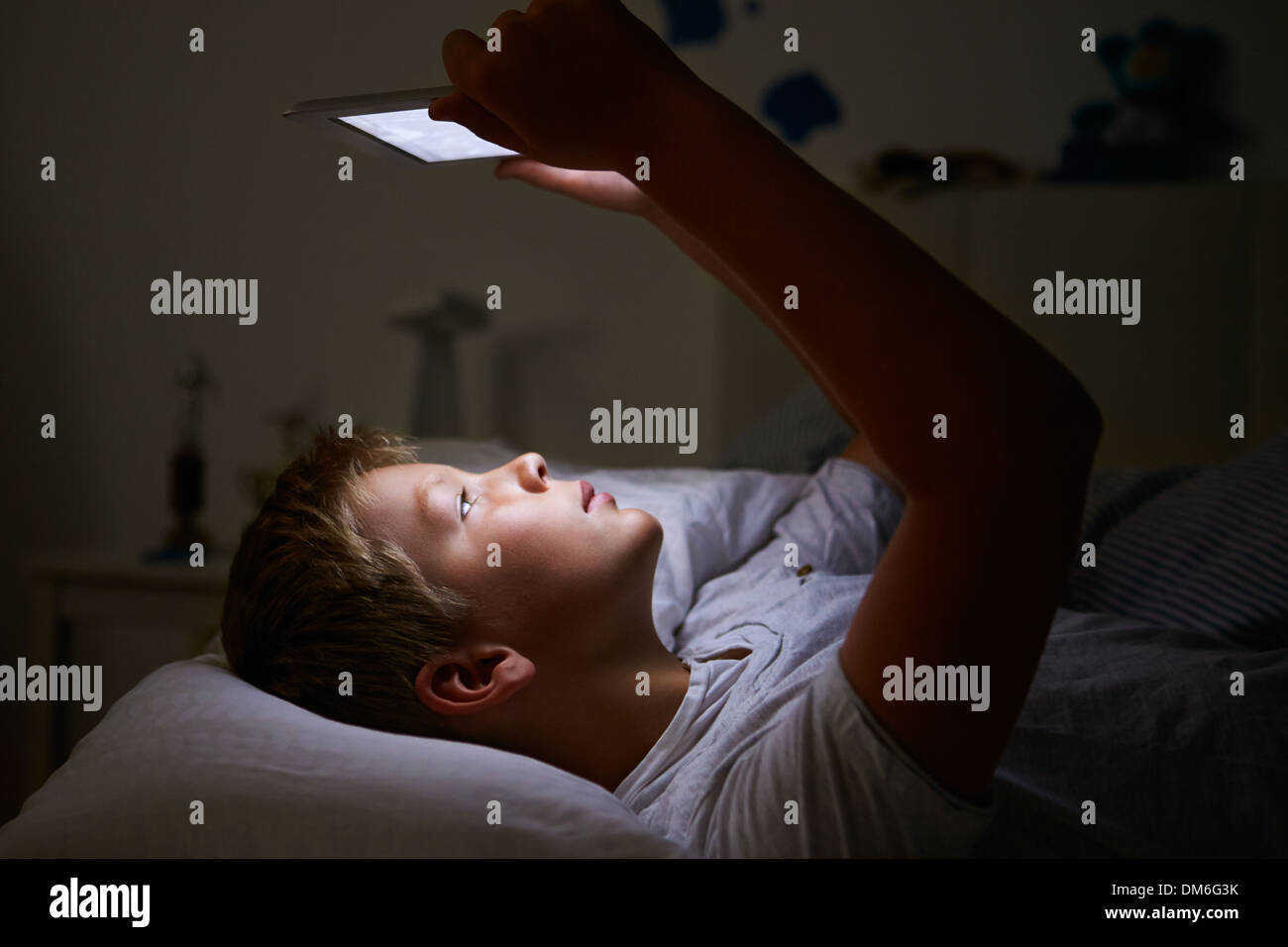 Boy Looking At Digital Tablet In Bed At Night Stock Photo