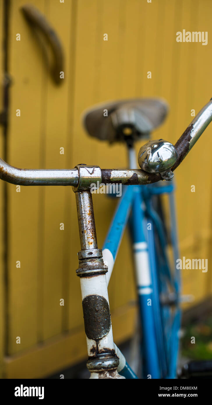 Old blue bike parked against a yellow shed Stock Photo