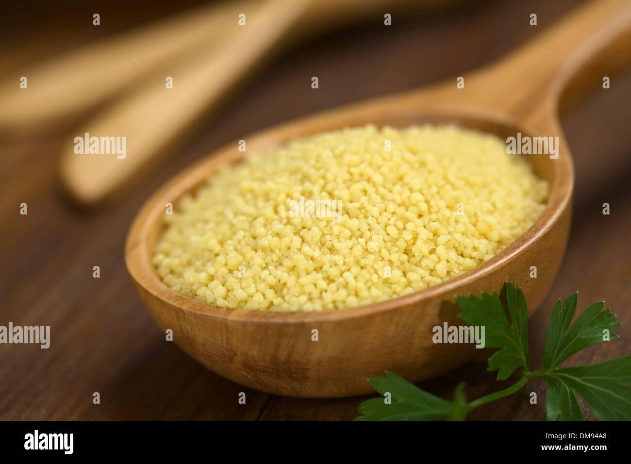Raw couscous on wooden spoon with parsley leaf on the side (Very Shallow Depth of Field, Focus one third into the couscous) Stock Photo