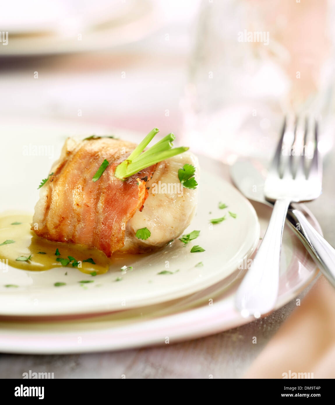 monk fish fillet wrapped in bacon served with a sauce and a garnish of parsley, on a white plate brightly lit Stock Photo
