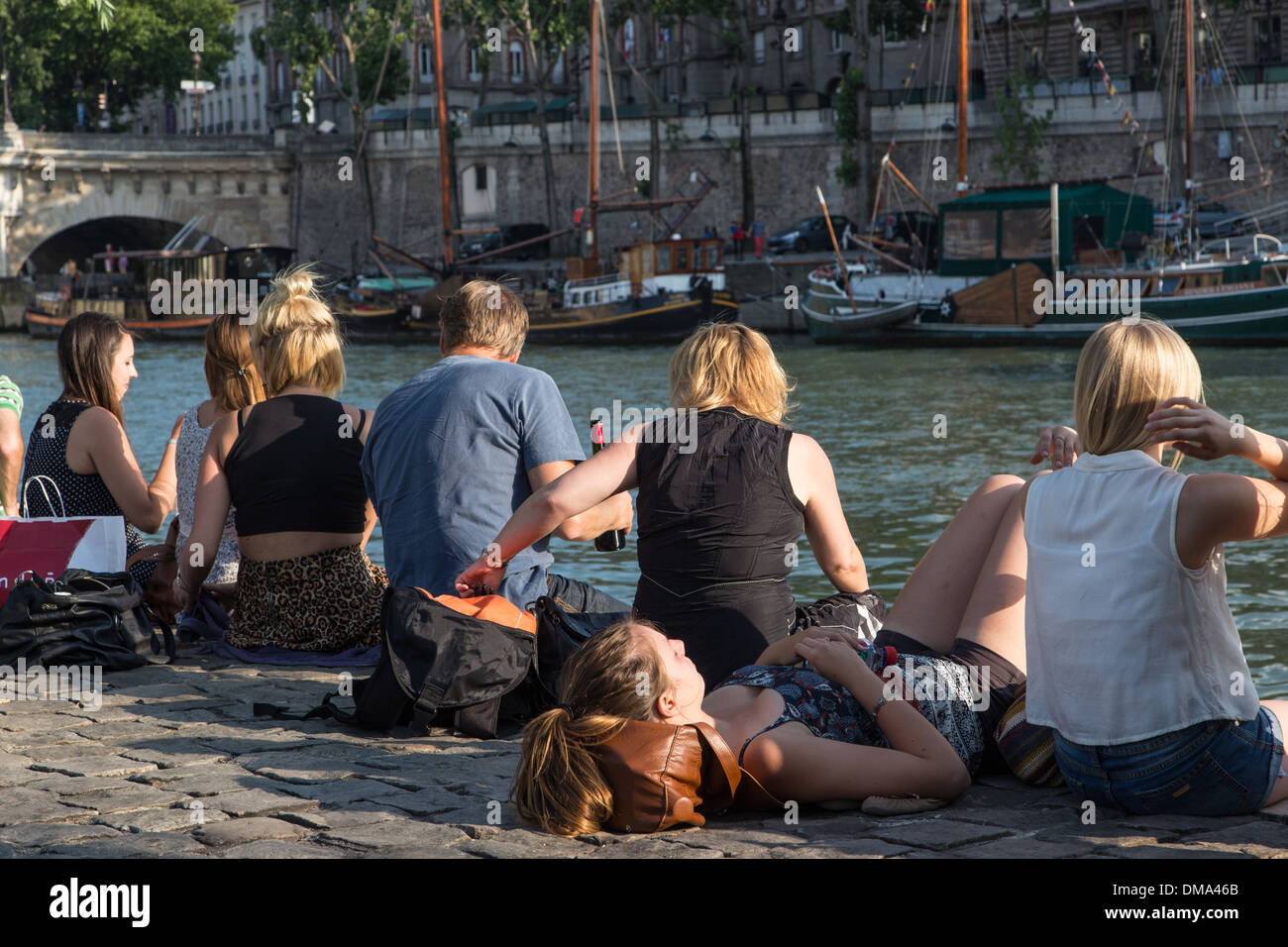 RELAXING AND PICKNICKING ON THE QUAYS OF THE SEINE, ILE DE LA CITE WITH THE PONT NEUF BRIDGE AND SAILBOATS IN FRONT OF THE SQUARE DU VERT GALANT, QUAY OF THE LOUVRE, PARIS (75), FRANCE Stock Photo