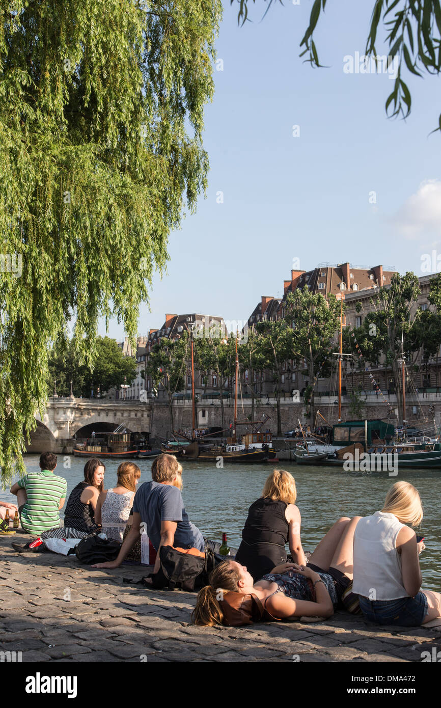 RELAXING AND PICNICKING ON THE QUAYS OF THE SEINE, ILE DE LA CITE WITH THE PONT NEUF BRIDGE AND SAILBOATS IN FRONT OF THE SQUARE DU VERT GALANT, QUAY OF THE LOUVRE, PARIS (75), FRANCE Stock Photo