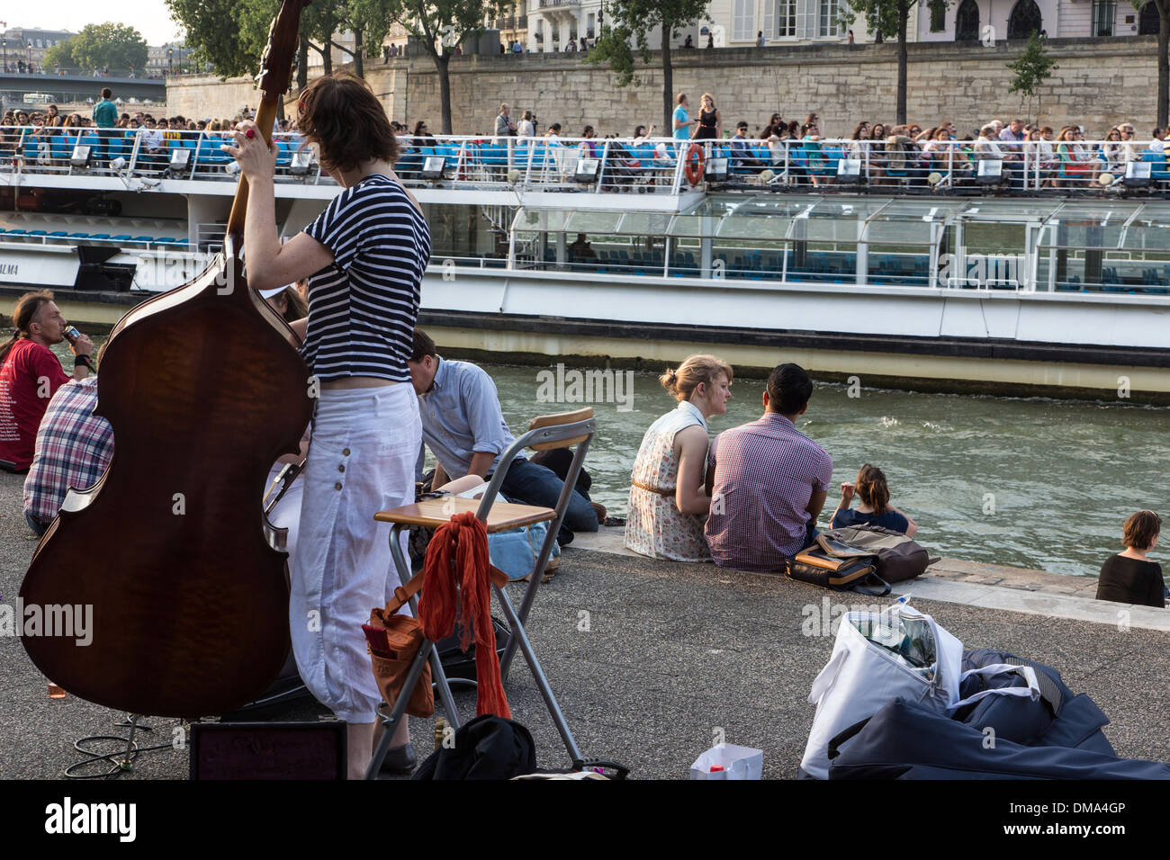 YOUTHS RELAXING WITH MUSIC (DOUBLE BASS) BY THE SEINE ON THE QUAY DE LA TOURNELLE, WITH A HOUSEBOAT AND THE LA TOURNELLE BRIDGE, PARIS (75), FRANCE Stock Photo
