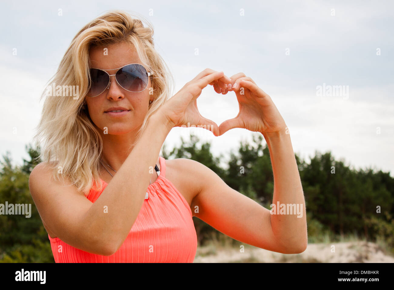 woman face portrait 'hands heart' 'hands heart shape' 'heart shape' 'woman sunglasses' overcast :gray sky' summer blond Stock Photo