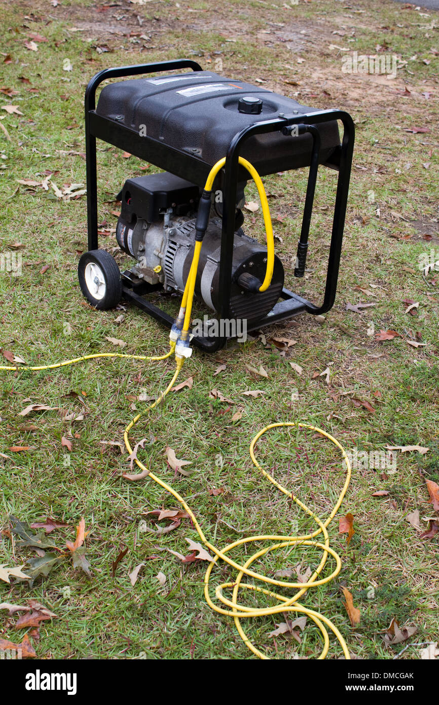 Portable electric generator with power cords attached sits on grass. Stock Photo