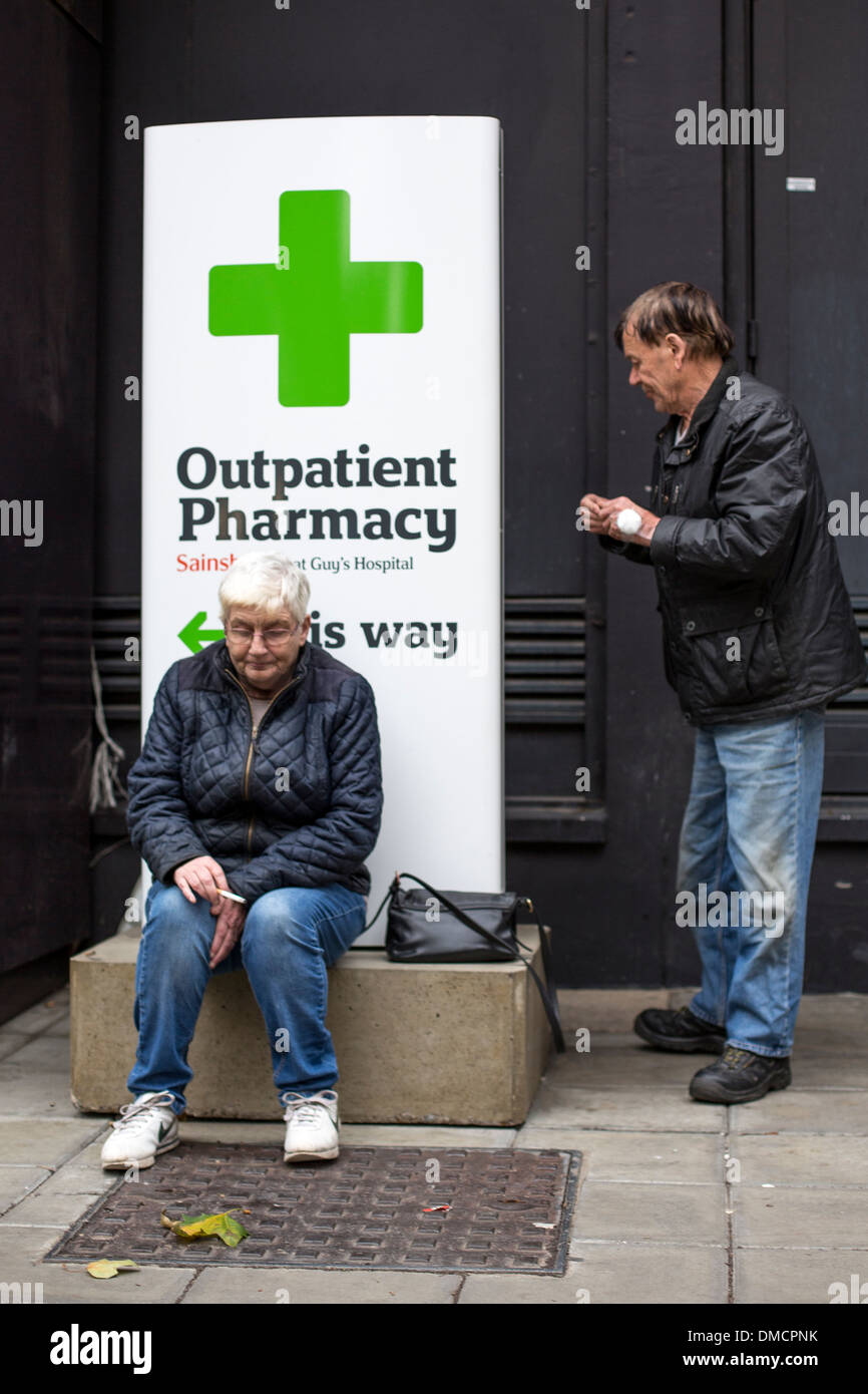 Man and woman smoking cigarettes next to outpatient pharmacy sign Stock Photo