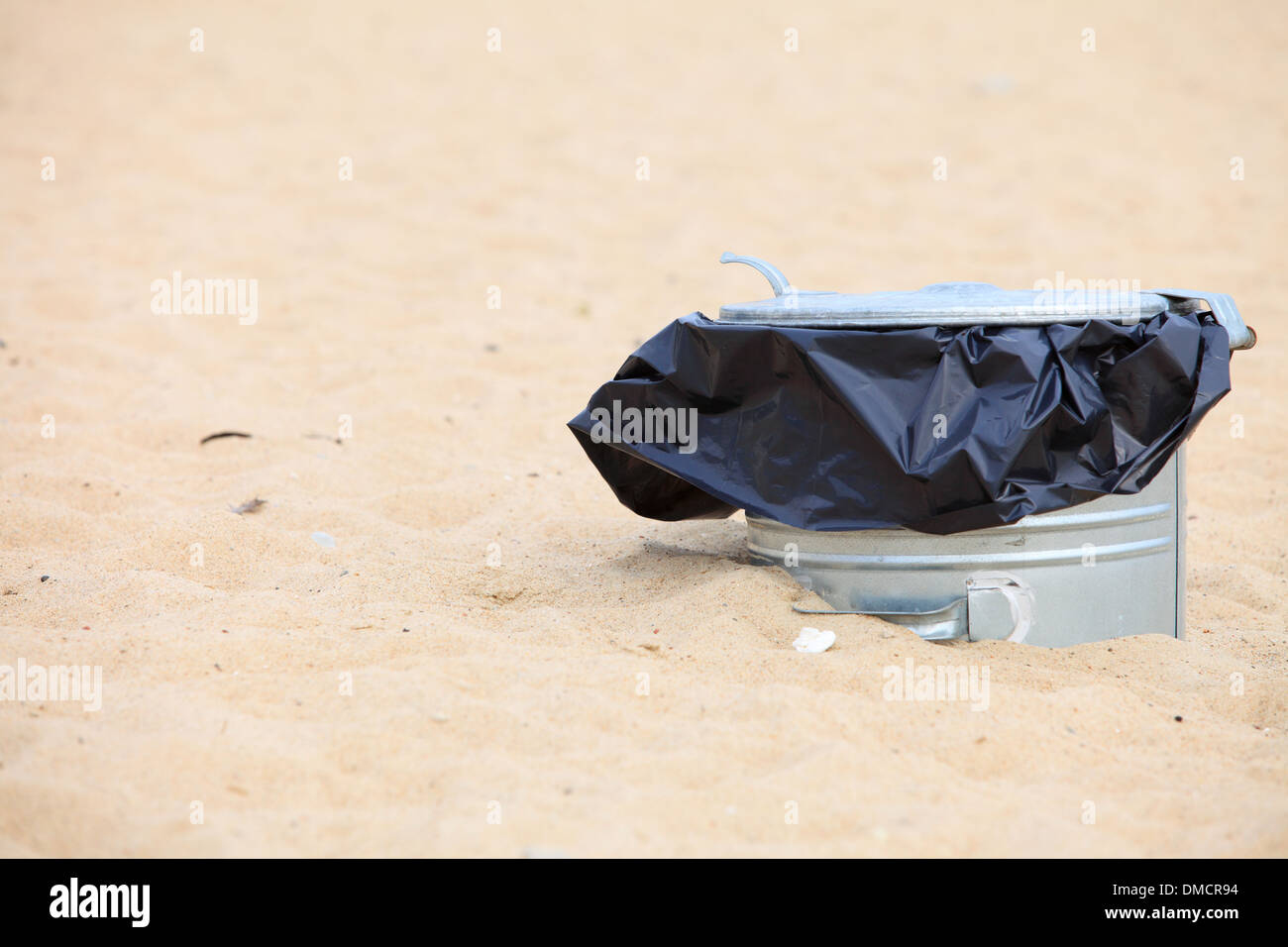 Gray metal garbage bin or trash can with a plastic bag inside beach