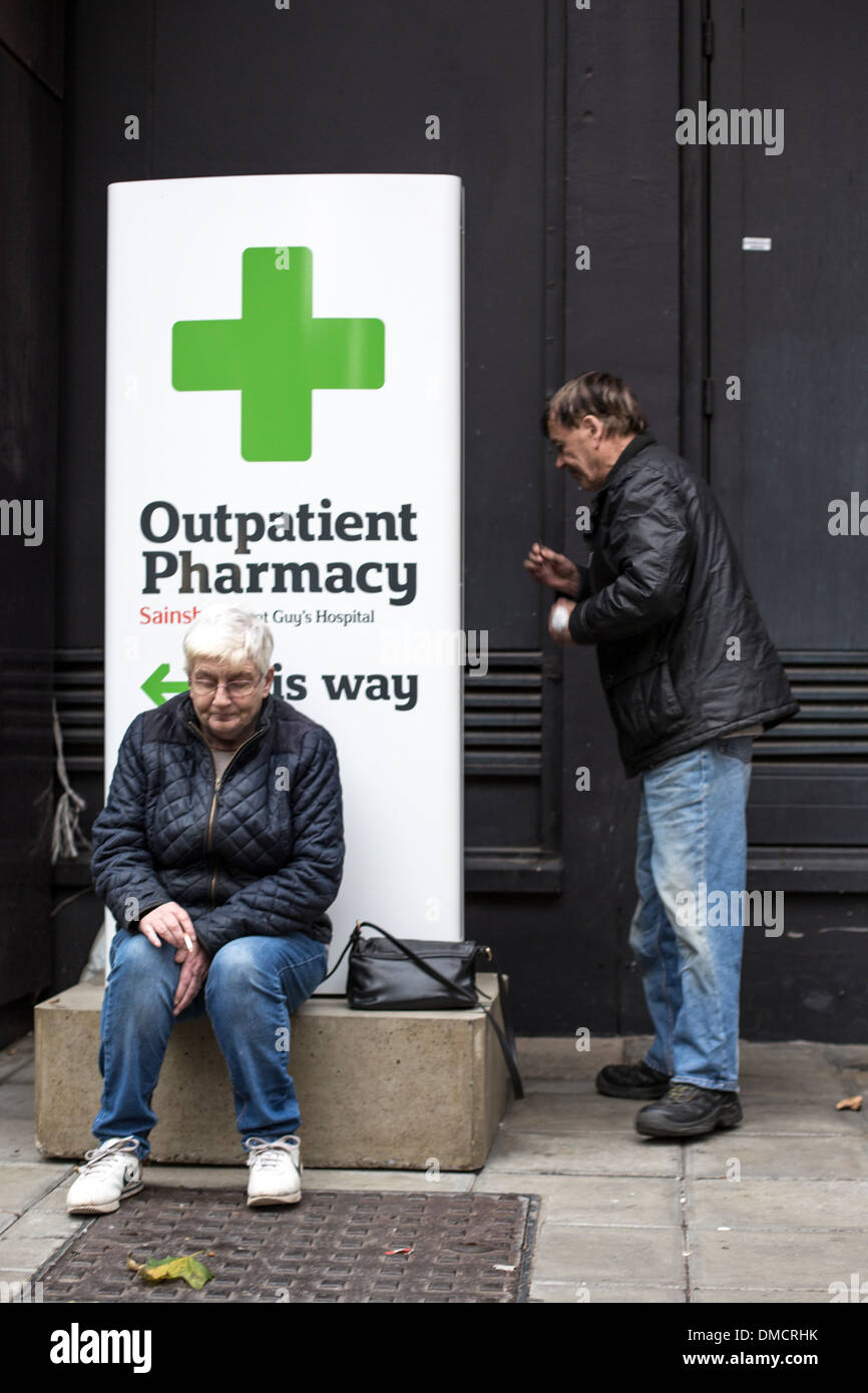 Man and woman smoking next to outpatient pharmacy sign at hospital. Stock Photo