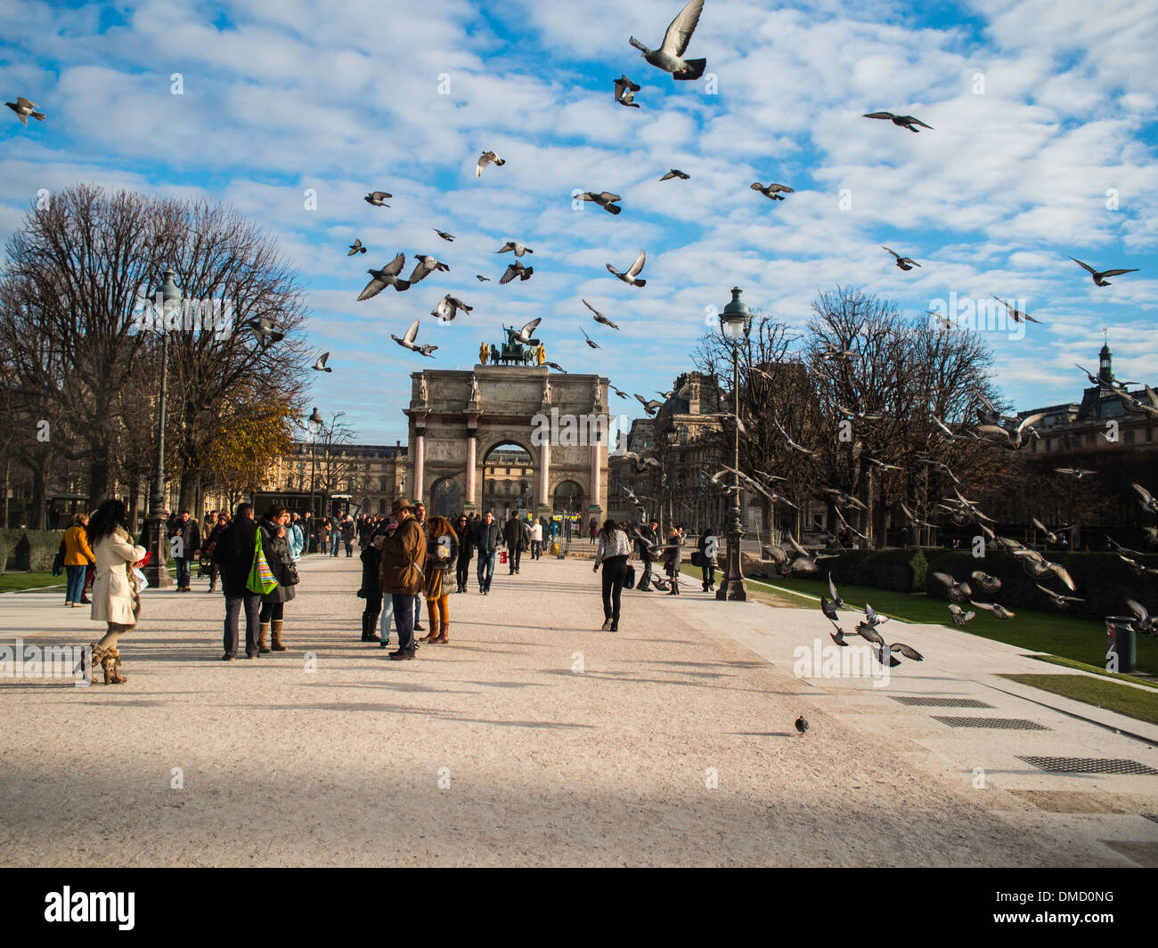 Pigeons fly by tourists close to Carrousel du Louvre arch Stock Photo