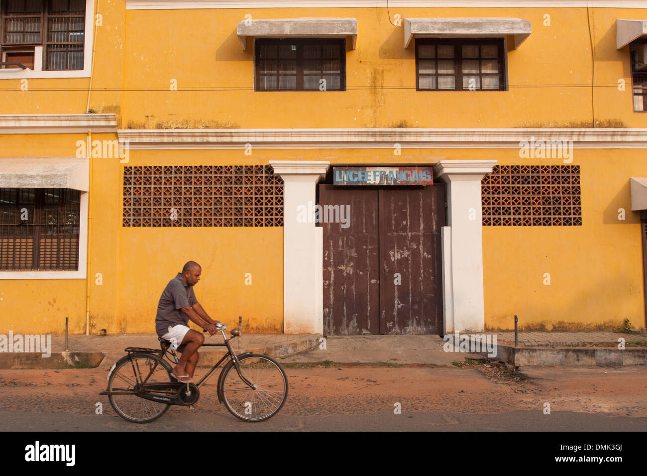 INDIAN ON A BICYCLE PASSING IN FRONT OF THE FACADE OF THE LYCEE FRANCAIS OF PONDICHERRY, FRENCH QUARTER, FORMER FRENCH TRADING POST OF PONDICHERRY, PUDUCHERRY, CAPITAL OF THE TERRITORY OF PONDICHERRY, INDIA Stock Photo