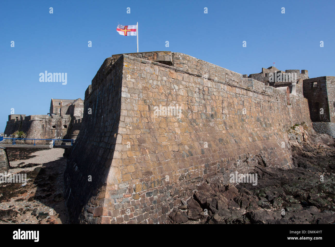 THE OUTER WALL OR BAILEY OF CASTLE CORNET, 13TH CENTURY FORTRESS, WITH THE GUERNSEY FLAG FLOATING IN THE WIND, SAINT PETER PORT, GUERNSEY, CHANNEL ISLANDS Stock Photo