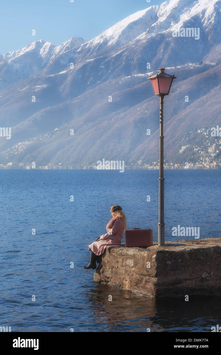 a woman in a pink coat is sitting on a jetty at a lake Stock Photo - Alamy