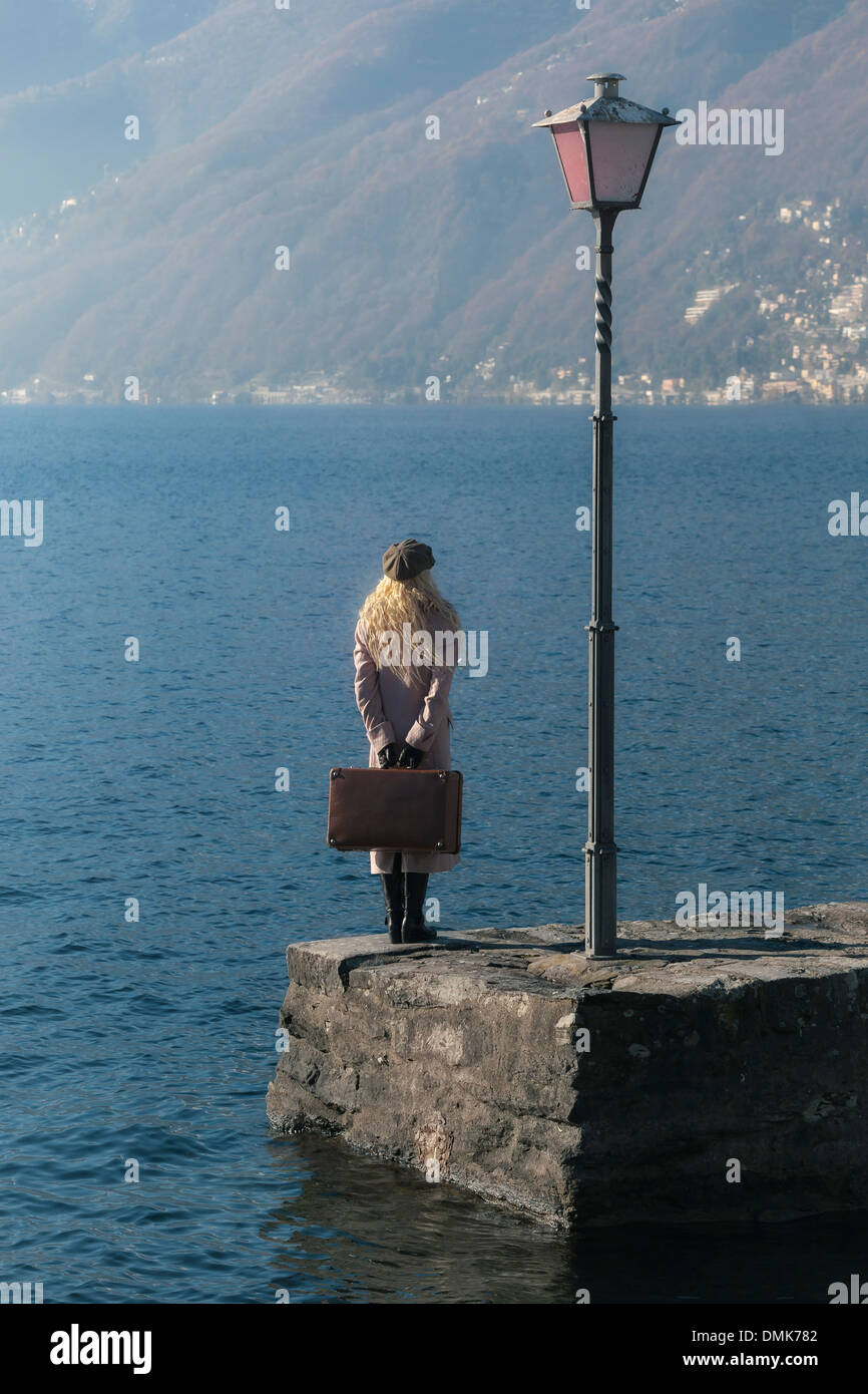 a woman in a pink coat is standing on a jetty at a lake Stock Photo
