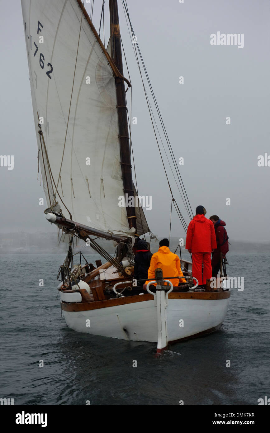 Gaff rigged sloop with sails on starboard tack sails into dense fog Stock Photo