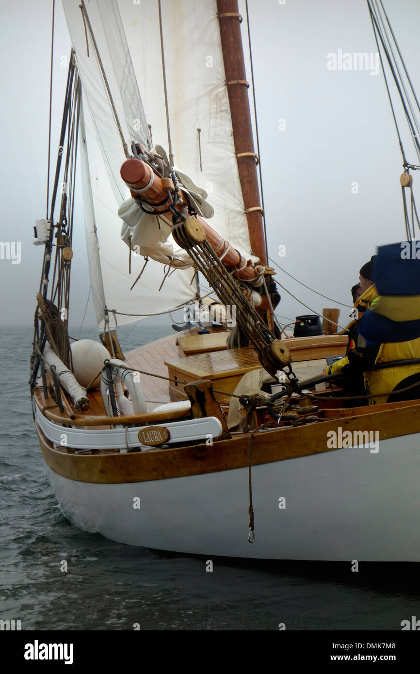 Classic wooden sloop with sails on starboard tack sails away into dense fog Stock Photo