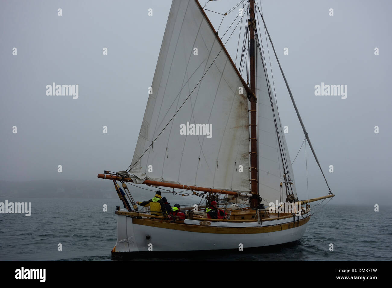 Gaff rigged sloop with sails on starboard tack sails into dense fog Stock Photo