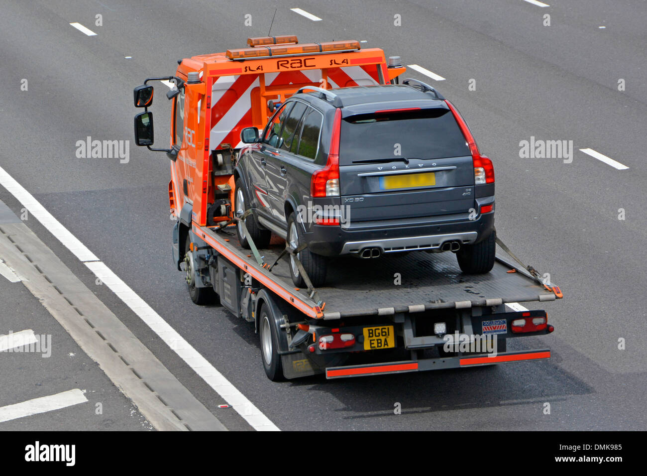 Aerial back rear side view of RAC breakdown truck rescue business transporting a Volvo car driving along M25 UK motorway road Essex England UK Stock Photo
