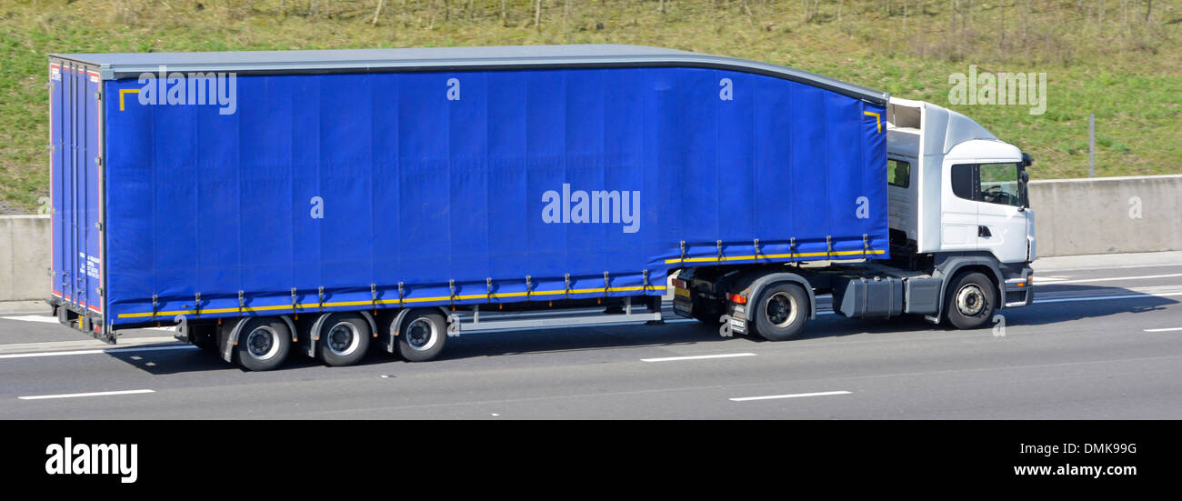Side view white hgv semi truck and driver with blue clean unmarked articulated soft sided folding curtain delivery trailer on m25 UK motorway road Stock Photo