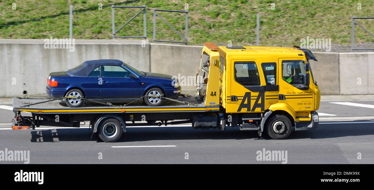 Side view AA rescue transporter breakdown assistance transport & recovery lorry truck transporting car on UK motorway Essex England UK Stock Photo