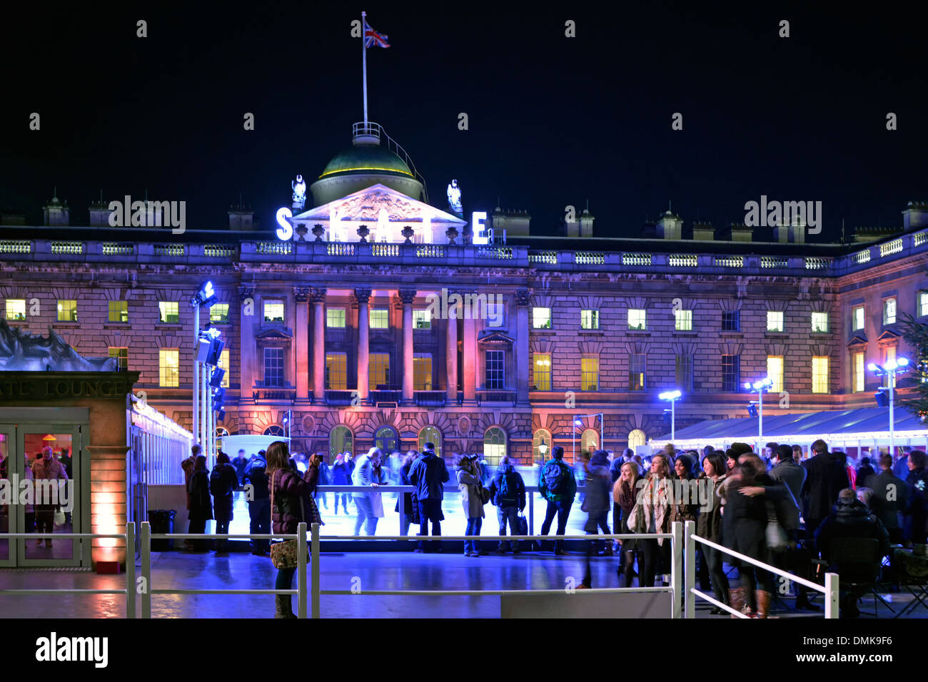 People watch ice skaters Somerset House night floodlit facade of historical building around temporary winter ice skating rink in courtyard London UK Stock Photo