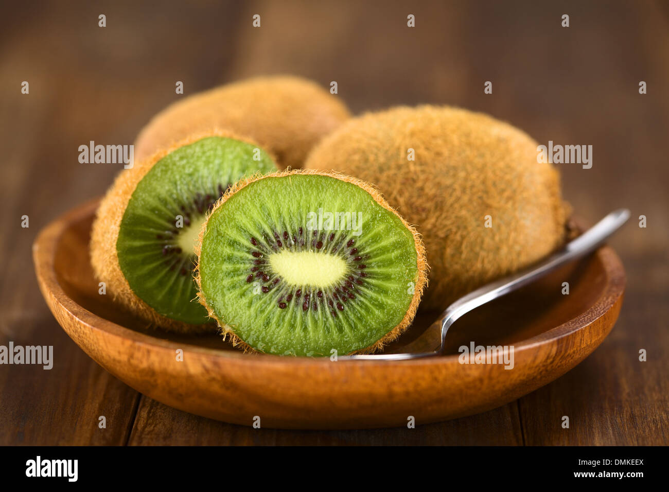 Kiwifruits on wooden plate with spoon (Selective Focus, Focus on the half kiwi) Stock Photo