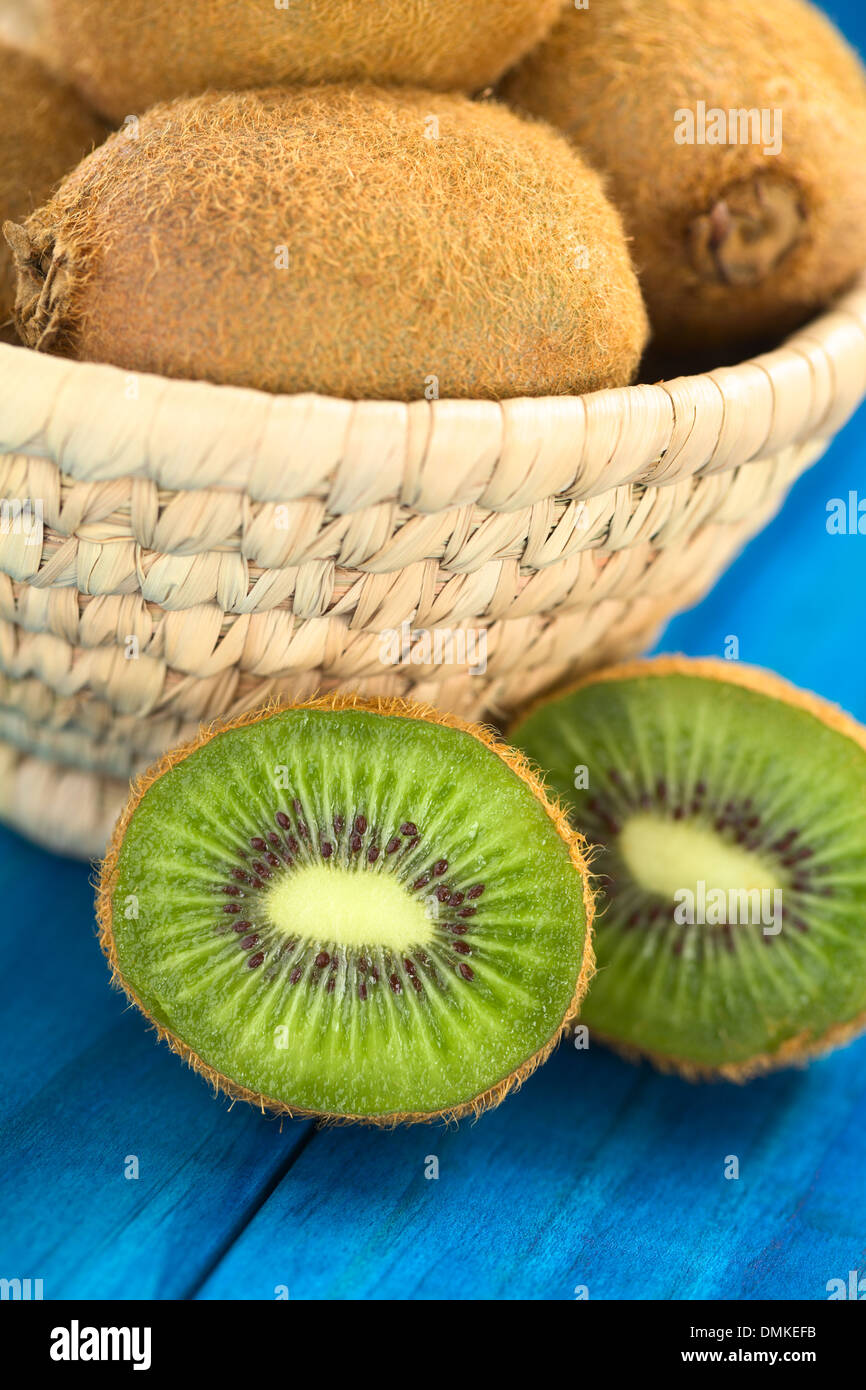 Half kiwi fruits on blue wood with kiwi fruits in basket behind (Selective Focus, Focus on the first half kiwi) Stock Photo