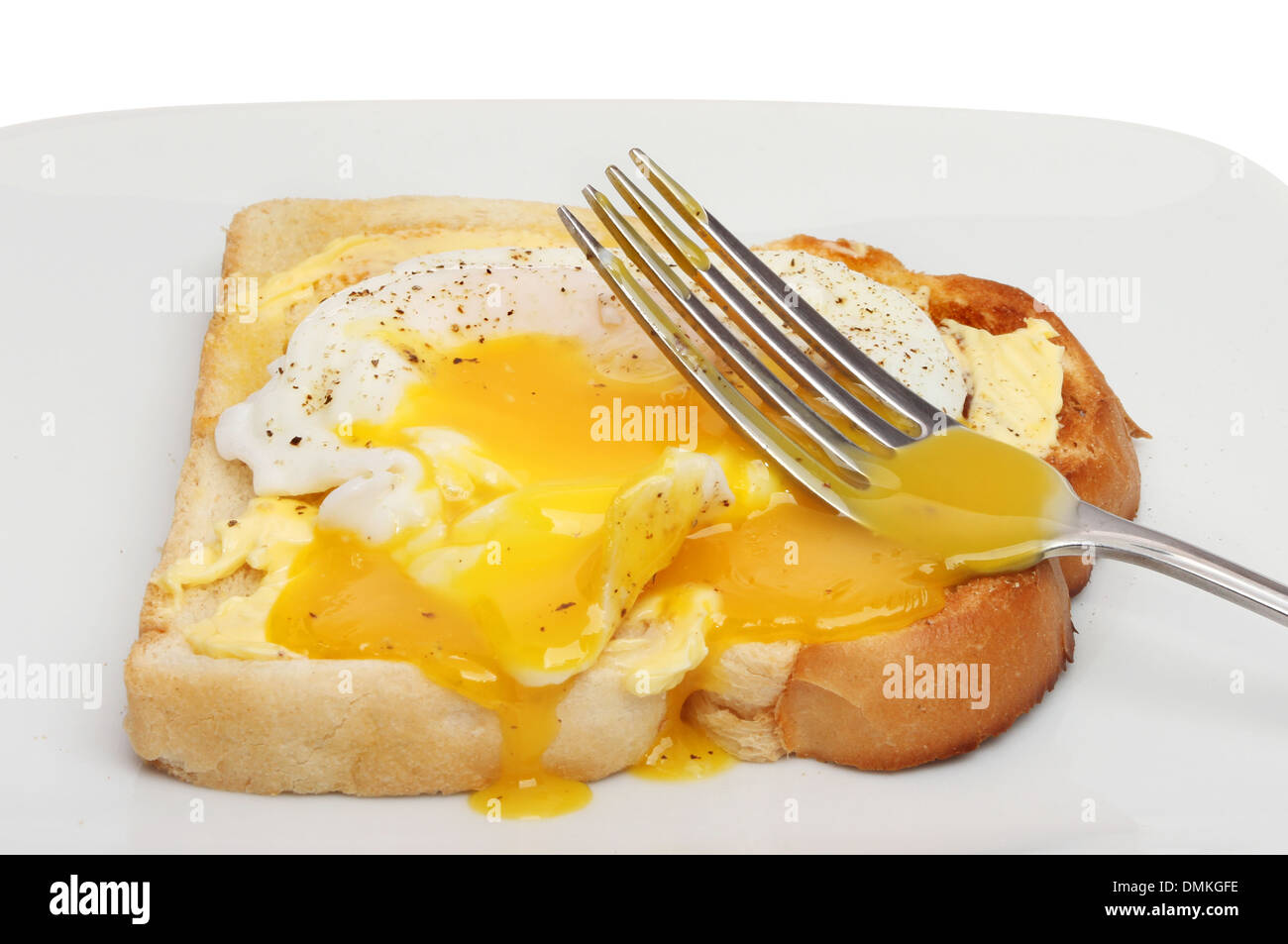 Closeup of a fork in the runny yolk of a poached egg on toast Stock Photo