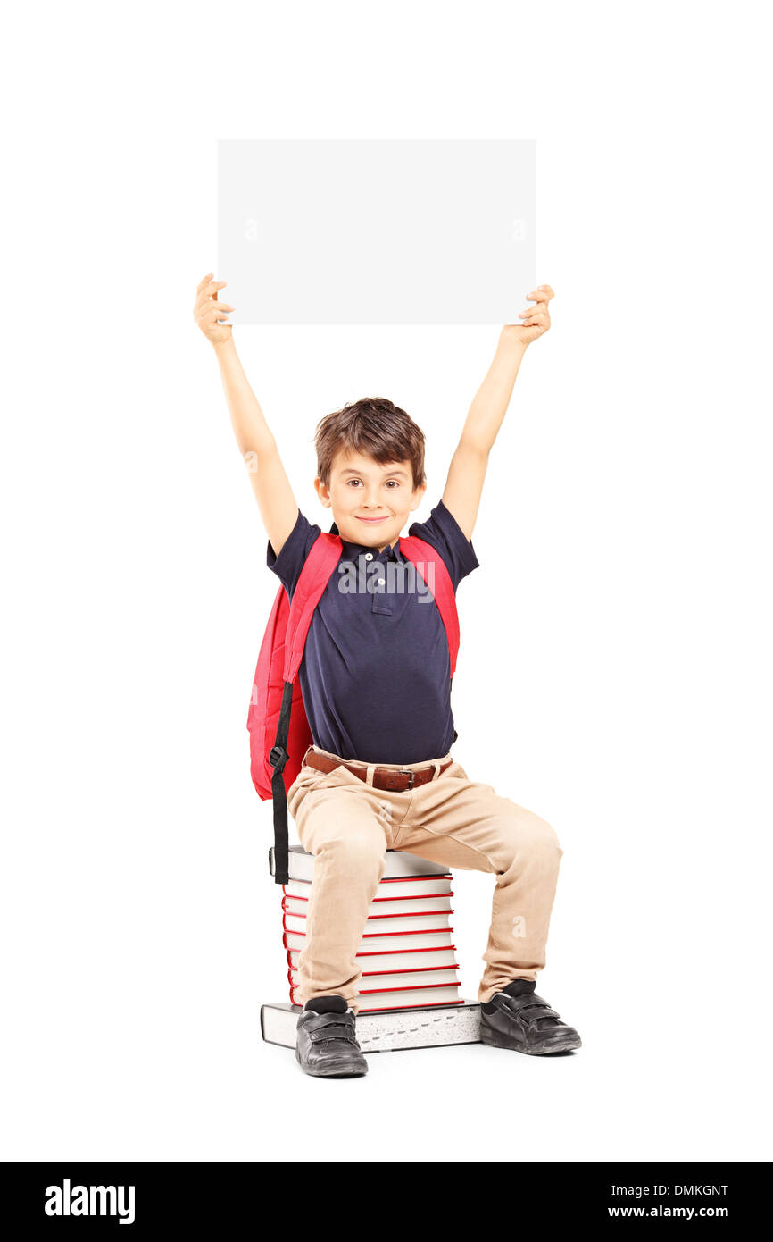 Happy schoolboy holding a blank panel above his head, seated on a pile of books Stock Photo