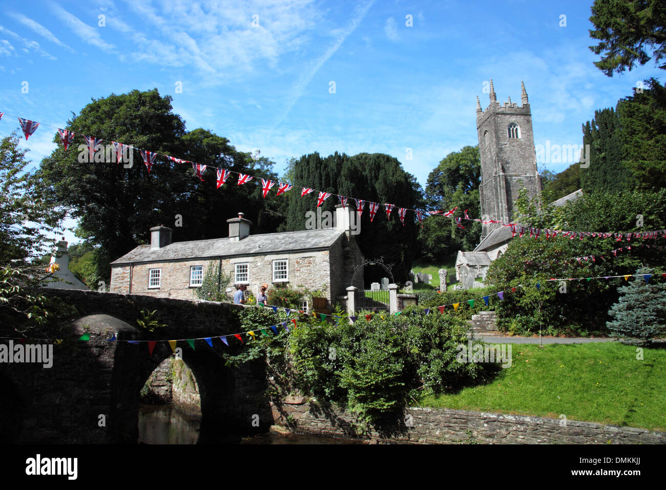 A row of stone cottages with a tall church tower and a bridge under a canopy of trees. Stock Photo