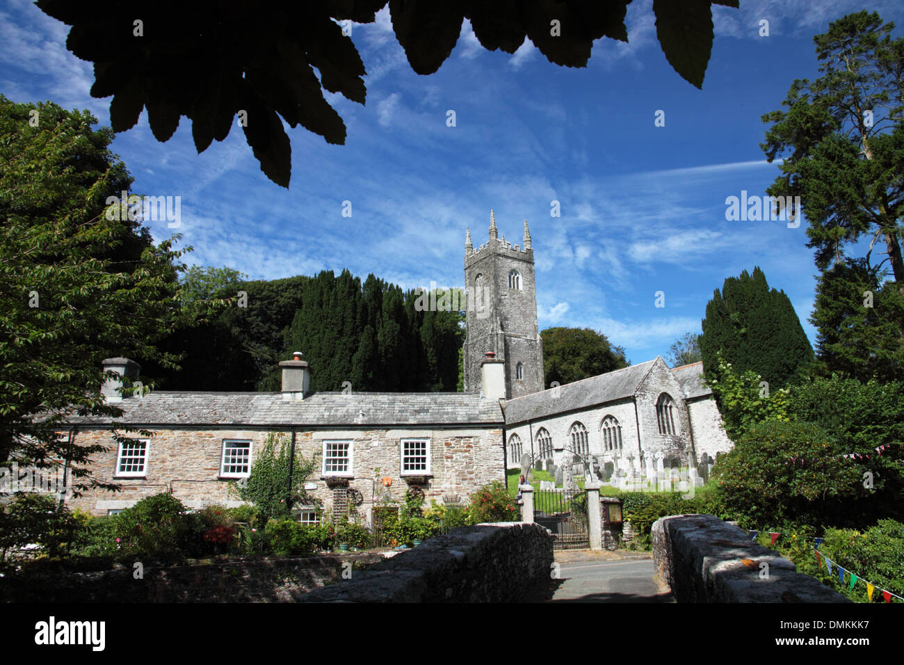 A row of stone cottages with a tall church tower under a canopy of trees. Stock Photo