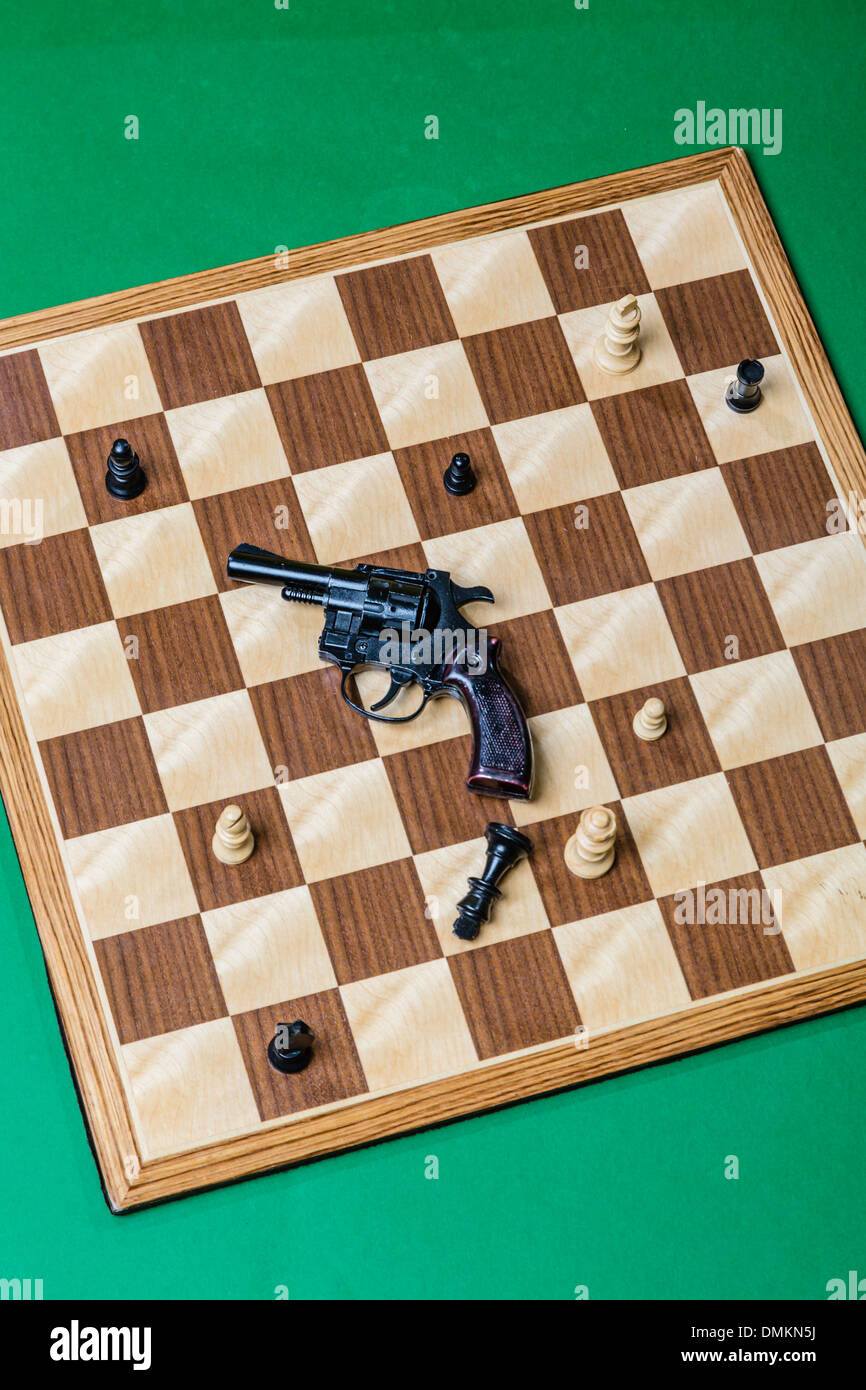 Chess board from above with gun on it.  Black king on its side.  Suitable for book cover or poster. Stock Photo