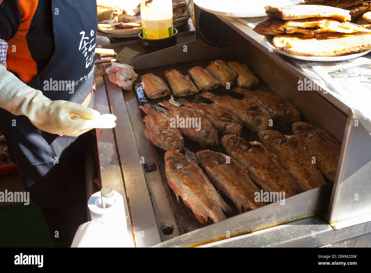 Woman frying fresh whole fish on griddle at Jagalchi shijang (traditional outdoor market) - Busan, South Korea Stock Photo