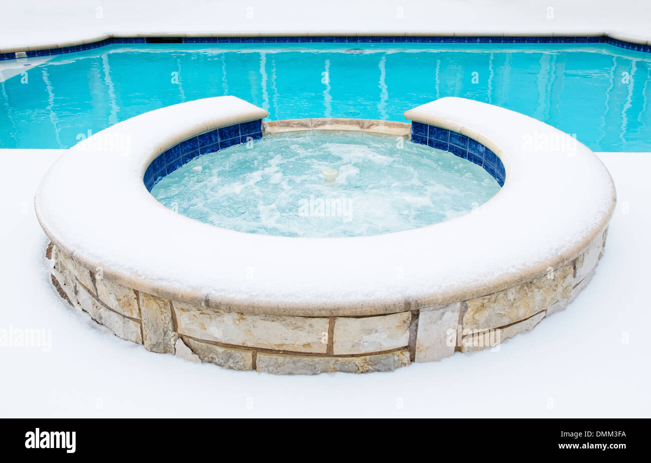 Outdoor residential hot tub or spa by swimming pool surrounded by snow in the winter Stock Photo