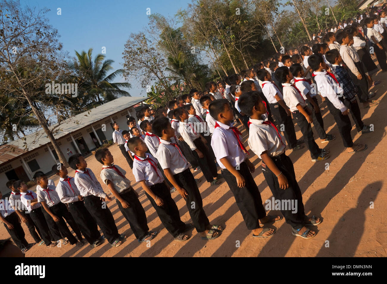 Horizontal angular view of school children standing to attention during their flag raising at a school in Laos. Stock Photo