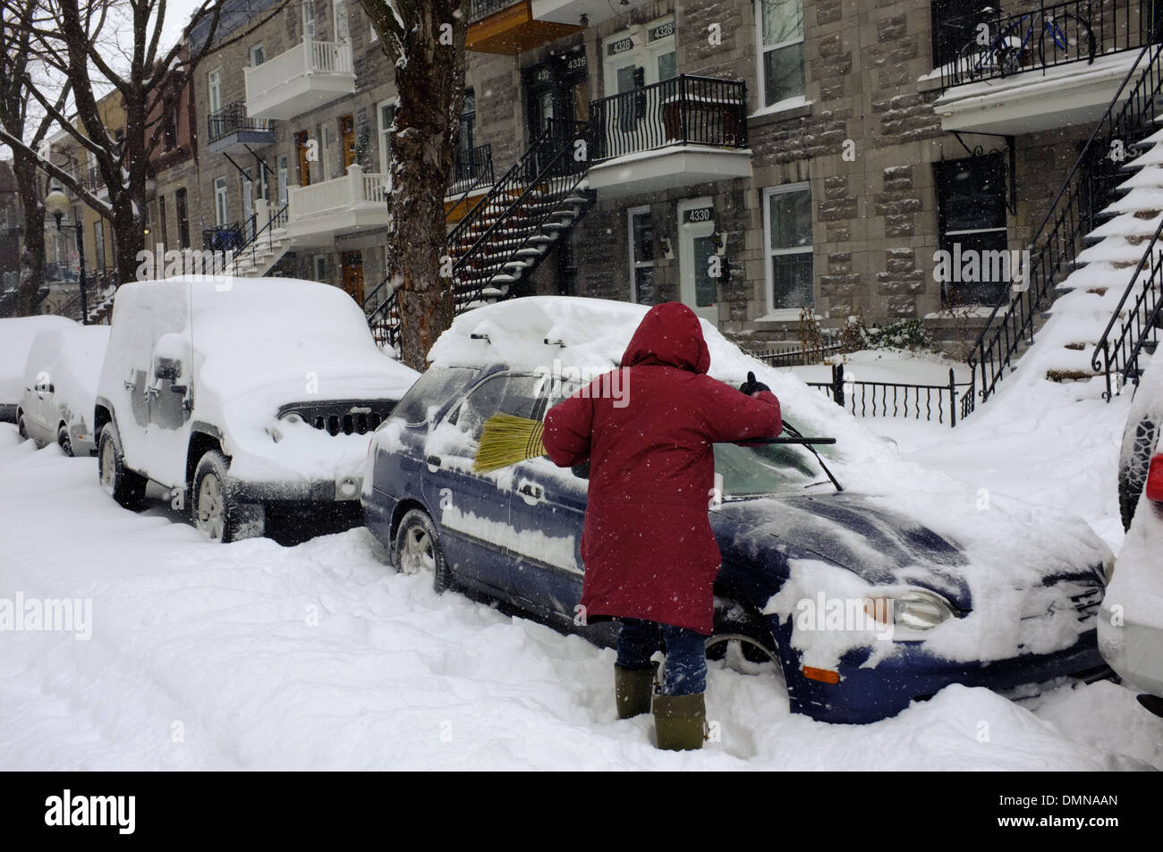 A woman clearing snow off her car with a broom in Montreal, Quebec
