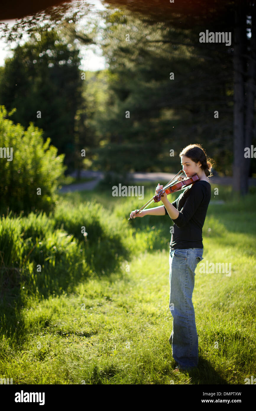 Lovely young brunette woman in jeans plays her violin in the balmy and beautiful afternoon sunlight on the bayou. Stock Photo