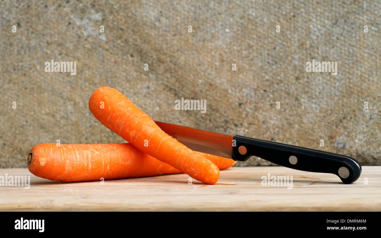Fresh carrots and kitchen knife on wooden cutting board. Stock Photo