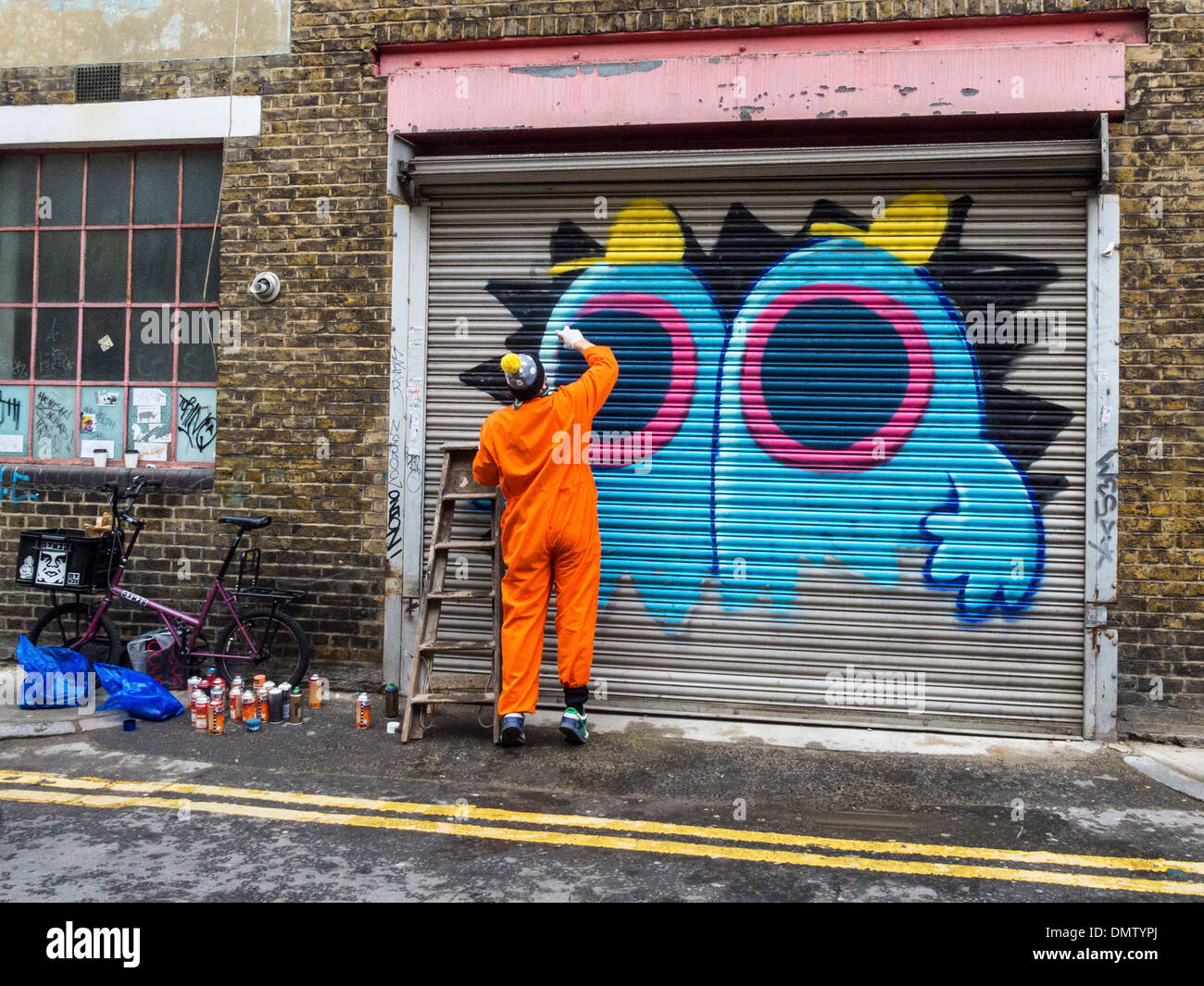 Street artist, Ronzo, at work. Artist uses spray paints to paint giant graffiti monster on a door - Fashion Street, London, UK Stock Photo