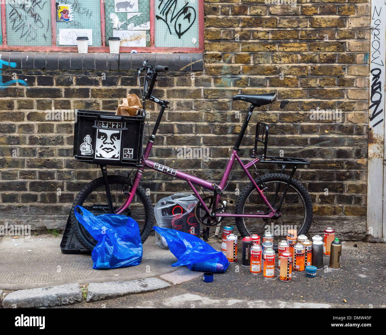 Street artist, Ronzo, at work. The bicycle and spray paints of the graffiti artist  - Fashion Street, London, UK Stock Photo