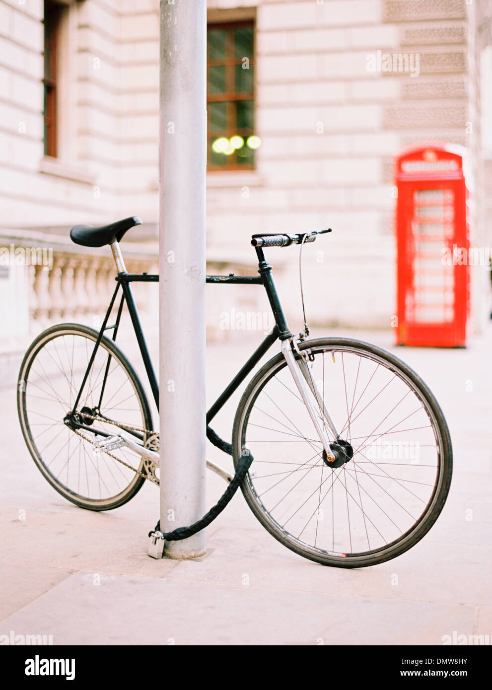 A bicycle chained and locked to a lamppost on a London street. A red public telephone box in background. Stock Photo