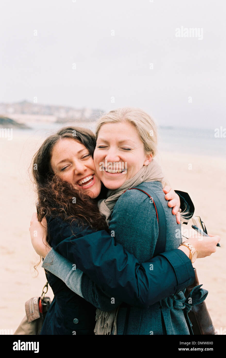 Two women cheek to cheek hugging on a beach. Stock Photo