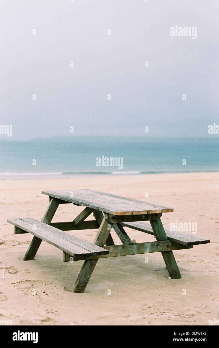 A wooden picnic bench on  sand. View out to sea. Stock Photo