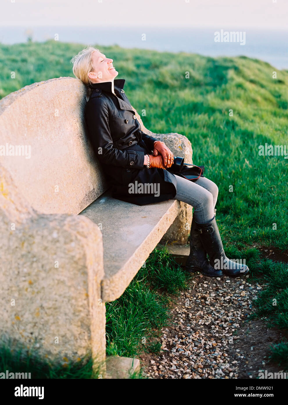 A woman seated on a stone bench on a coastal path. Stock Photo