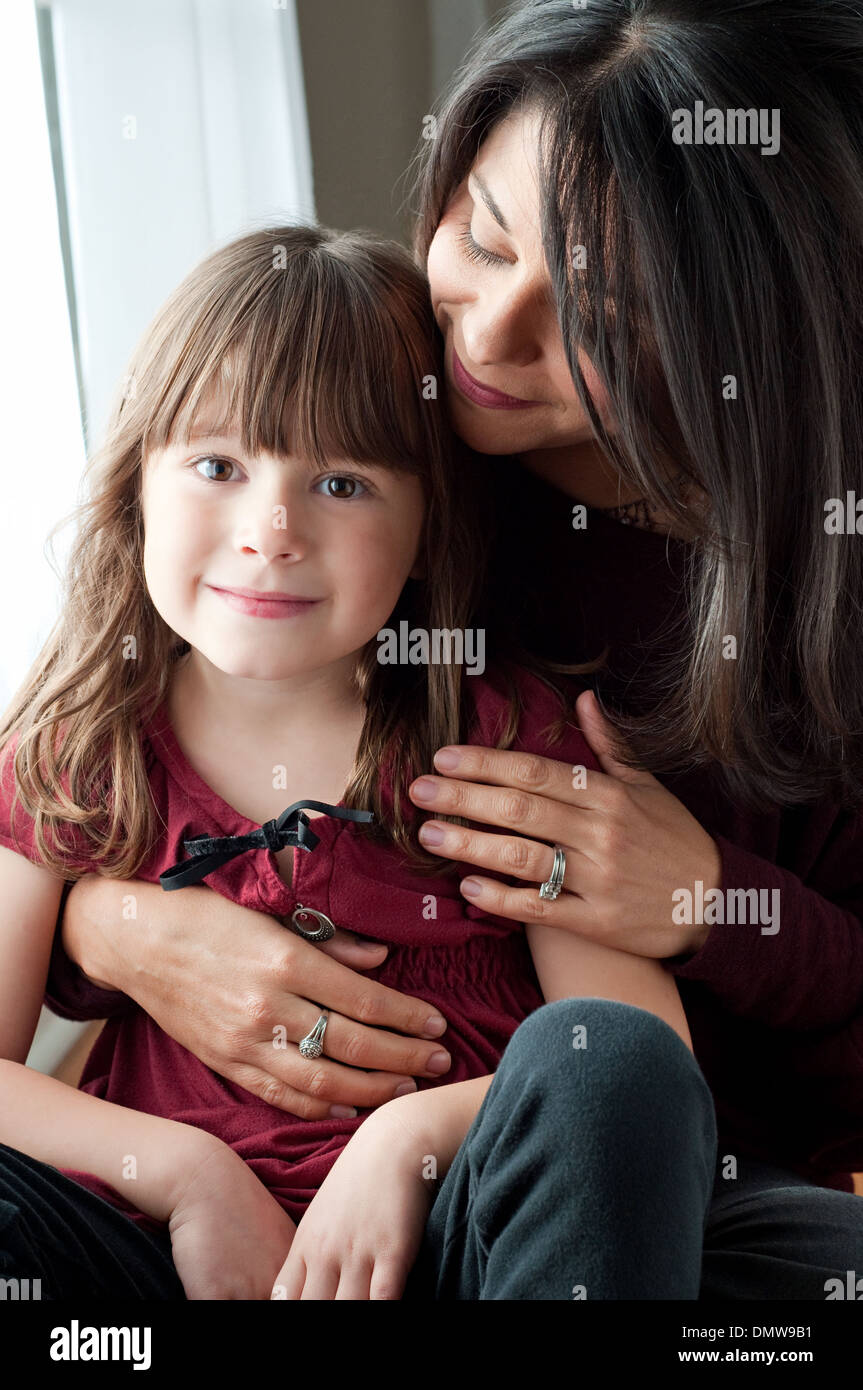 A beautiful Hispanic woman holds her beautiful daughter, smiling. A multiracial mother and daughter family portrait. Stock Photo