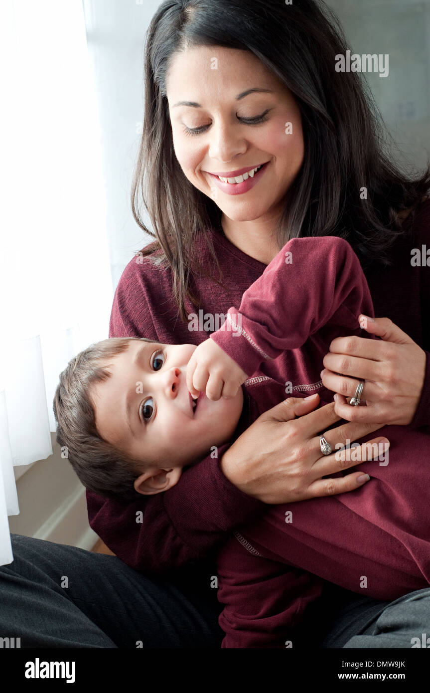 A beautiful Hispanic woman holds her playful son, smiling. A multiracial mother and son family portrait. Stock Photo