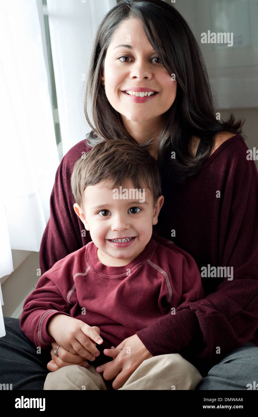 A beautiful Hispanic woman holds her son, smiling. A multiracial mother and son family portrait. Stock Photo