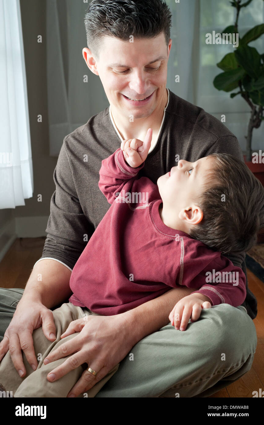A child sits in his father's lap, pointing his finger at his father who is smiling. A family portrait. Stock Photo