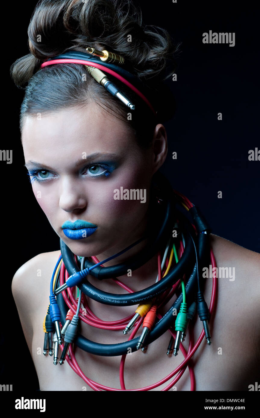A beautiful young woman with ombre blue makeup, electrical cord, music cables wrapped around her neck. An edgy beauty portrait. Stock Photo
