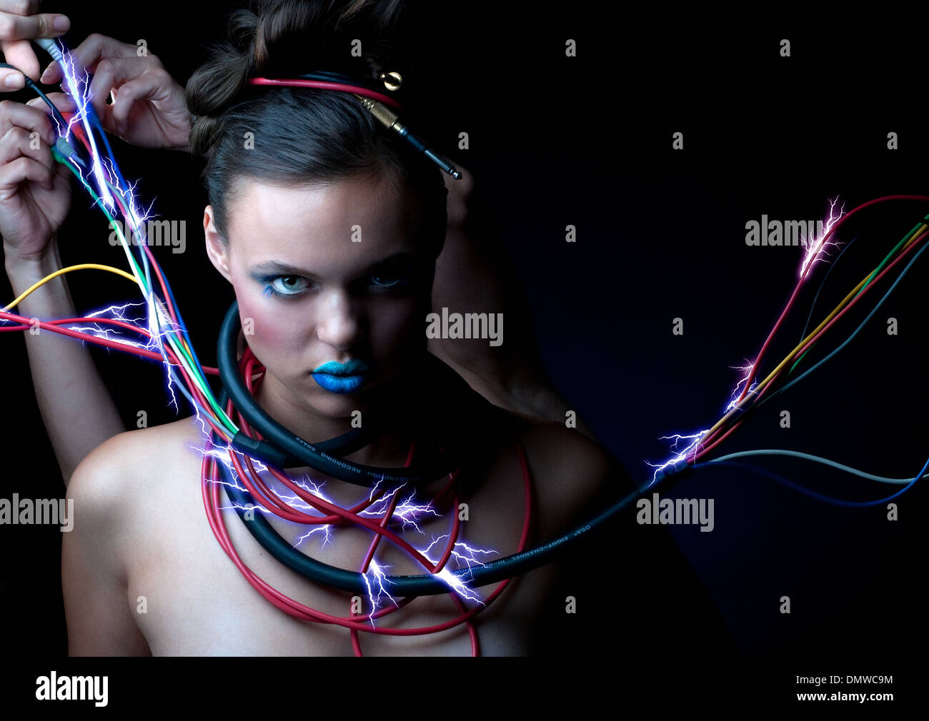 A robot like woman staring at camera with sparkling electric cables wrapped around her neck. Hands are adjusting cables. Stock Photo