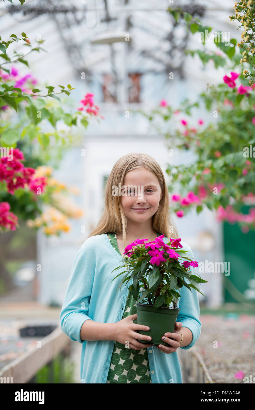 An organic flower plant nursery. A young girl holding a flowering plant. Stock Photo